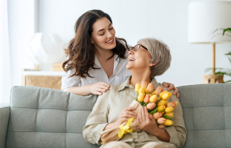 Beautiful young woman and her mother with flowers tulips in hands at home.の写真素材