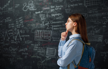 Back to school. Happy cute industrious teenager indoors. Girl is learning in class on background of blackboard.の写真素材
