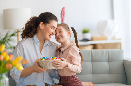 Happy holiday! Mother and her daughter with painting eggs. Family celebrating Easter. Cute little child girl is wearing bunny ears.の写真素材