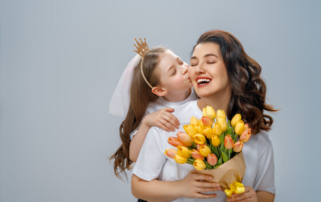 Happy women's day. Child is congratulating mom and giving her yellow flowers. Mum and girl smiling on light grey background. Family holiday and togetherness.の写真素材