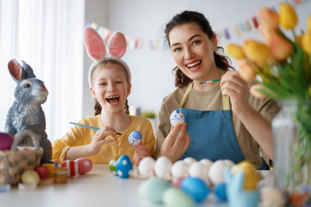 Mother and her daughter painting eggs. Happy family preparing for Easter. Cute little child girl wearing bunny ears.の写真素材