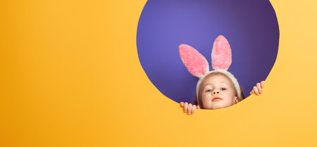 Cute little child wearing bunny ears on Easter day. Girl on bright purple and yellow background.