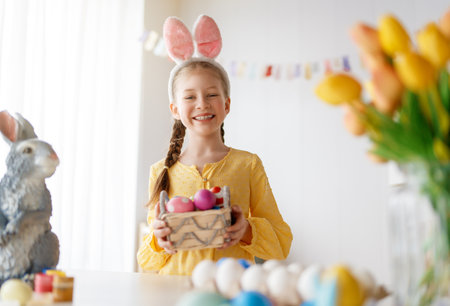 Beautiful child painting eggs. Happy family preparing for Easter. Cute little girl is wearing bunny...