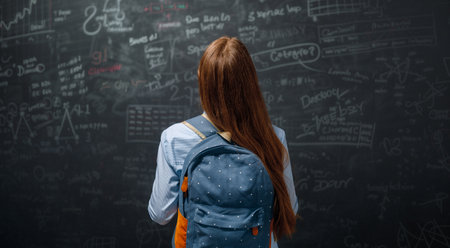 Back to school. Happy cute industrious teenager indoors. Girl is learning in class on background of blackboard.の写真素材