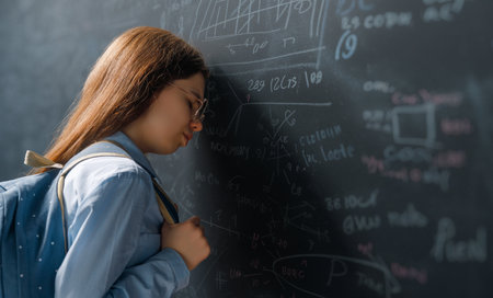 Back to school. Unhappy teenager indoors. Girl is learning in class on background of blackboard.
