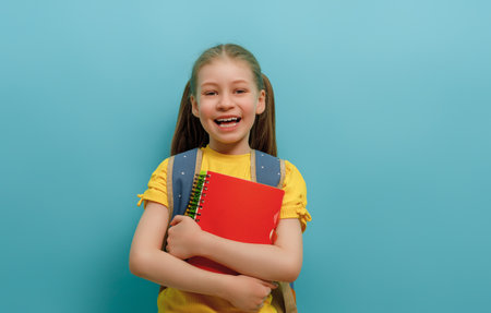 Cute happy kid standing on light blue background. Child with backpack, little girl is ready to back to school.の写真素材