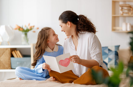 Happy mother's day. Child daughter is congratulating mom and giving her postcard. Mum and girl smiling and hugging. Family holiday and togetherness.の写真素材