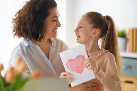 Happy mother's day. Child daughter is congratulating mom and giving her postcard. Mum and girl smiling and hugging. Family holiday and togetherness.の写真素材