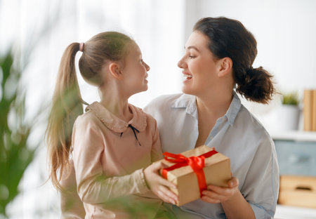 Happy mother's day. Child daughter is congratulating mom and giving her gift box. Mum and girl smiling and hugging. Family holiday and togetherness.の写真素材
