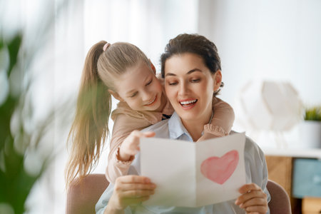 Happy mother's day. Child daughter is congratulating mom and giving her postcard. Mum and girl smiling and hugging. Family holiday and togetherness.の写真素材