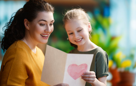 Happy mother's day. Child daughter is congratulating mom and giving her postcard. Mum and girl smiling and hugging. Family holiday and togetherness.の写真素材