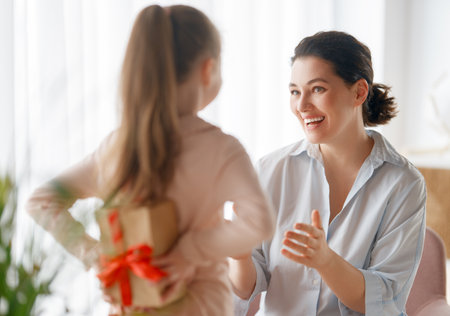 Happy mother's day. Child daughter is congratulating mom and giving her gift box. Mum and girl smiling and hugging. Family holiday and togetherness.の写真素材