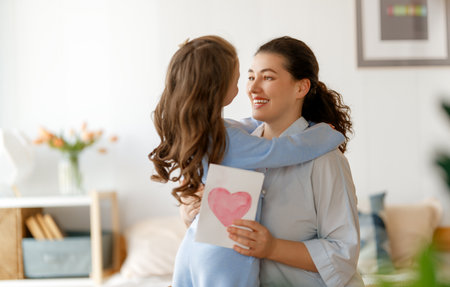 Happy mother's day. Child daughter is congratulating mom and giving her postcard. Mum and girl smiling and hugging. Family holiday and togetherness.の写真素材