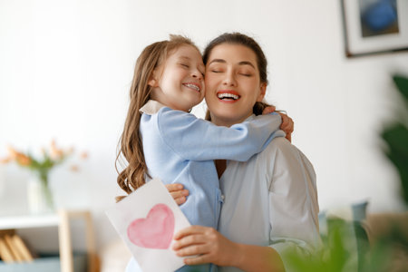 Happy mother's day. Child daughter is congratulating mom and giving her postcard. Mum and girl smiling and hugging. Family holiday and togetherness.の写真素材