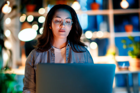 Young businesswoman working on laptop near window in the evening.の写真素材