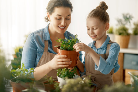 Cute child girl helping her mother to care for plants. Mom and her daughter engaging in gardening at home. Happy family in spring day.の写真素材