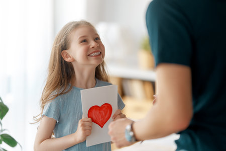 Child daughter is congratulating her father and giving him postcard. Girl is smiling. Family holiday and togetherness.の写真素材