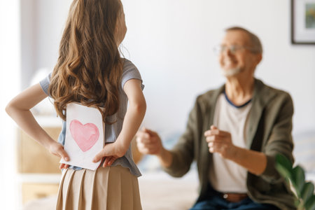 Child granddaughter is congratulating her grandfather and giving him postcard. Family holiday and togetherness.の写真素材