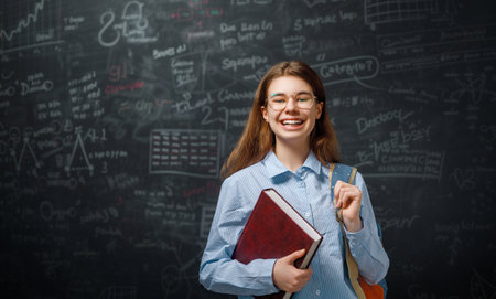 Back to school. Happy cute industrious teenager indoors. Girl is learning in class on background of blackboard.の写真素材