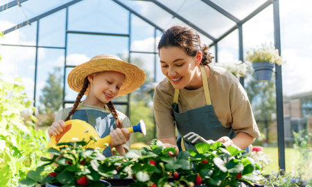 Happy mother and daughter are gardening in the greenhouse. Child is helping her mom and learning about botany.の写真素材