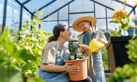 Happy mother and daughter are gardening in the greenhouse. Child is helping her mom and learning about botany.の写真素材