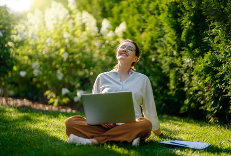 Happy woman working on laptop in summer morning sitting in the garden.の写真素材