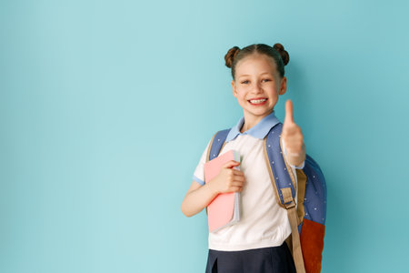 Cute happy teenager standing on bright light blue background. Child with backpack, girl is ready to back to school.の写真素材