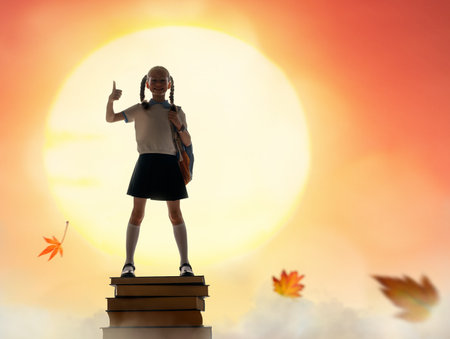 Back to school! Happy cute industrious child standing on the tower of books on background of sunset sky. Concept of education and reading. The development of the imagination.の写真素材
