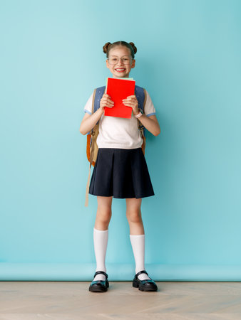 Cute happy teenager standing on bright light blue background. Child with backpack, girl is ready to back to school.の写真素材
