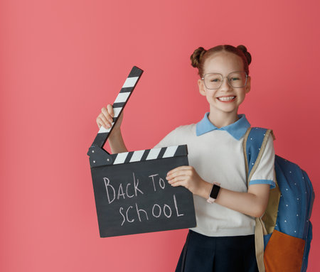 Cute happy teenager standing on pink background. Child with backpack, girl is ready to back to...