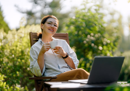 Happy woman working on laptop in summer morning sitting in the garden.の写真素材