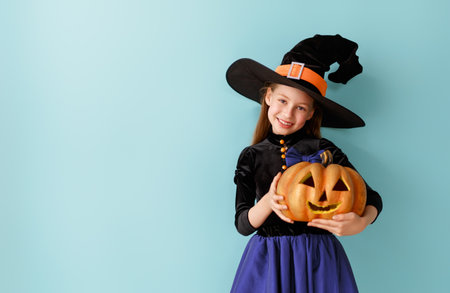 Beautiful laughing girl in witch costume with Halloween pumpkin on blue wall background.の写真素材