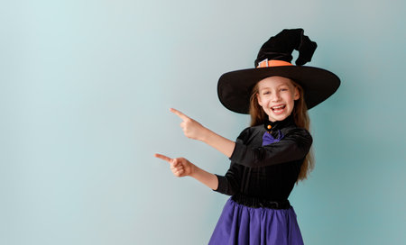 Beautiful laughing girl in Halloween witch costume on blue wall background.