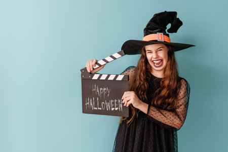Beautiful laughing girl in Halloween witch costume on blue wall background.の写真素材