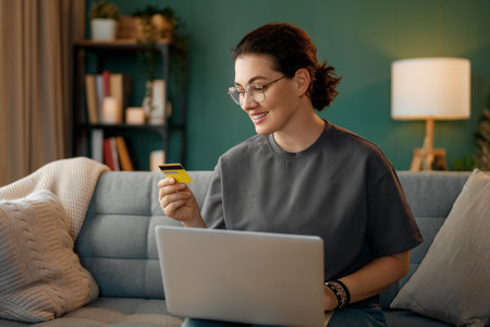 Woman is doing online purchases. Girl is doing shopping using laptop and credit card at home.の写真素材