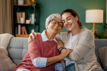 Beautiful mother and daughter are talking and smiling while sitting on couch at home.の写真素材
