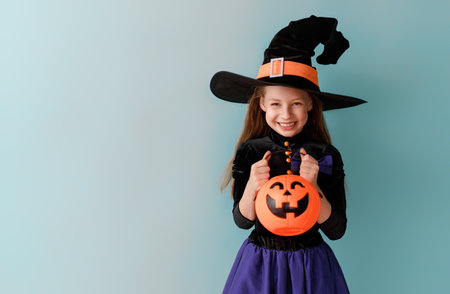 Beautiful laughing girl in witch costume with Halloween pumpkin on blue wall background.