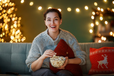 Merry Christmas and Happy New Year. Woman having fun near tree indoors. Girl watching holiday movies at home.の写真素材
