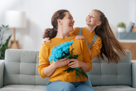 Happy women's day. Child daughter is congratulating mom and giving her flowers. Mum and girl smiling and hugging. Family holiday and togetherness.の写真素材