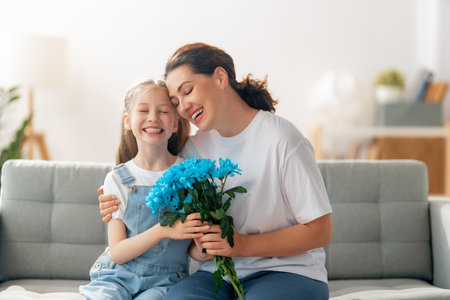 Happy women's day. Child daughter is congratulating mom and giving her flowers. Mum and girl smiling and hugging. Family holiday and togetherness.の写真素材
