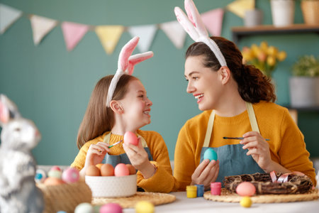 Mother and her daughter painting eggs. Happy family preparing for Easter. Cute little child girl wearing bunny ears.の写真素材