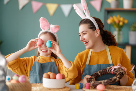 Mother and her daughter painting eggs. Happy family preparing for Easter. Cute little child girl wearing bunny ears.の写真素材