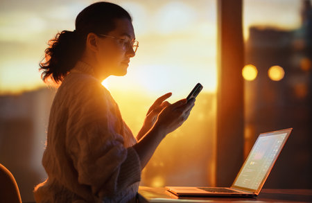 Young businesswoman working on laptop near window in the evening.の写真素材