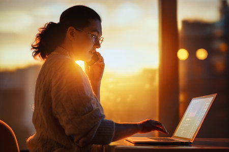 Young businesswoman working on laptop near window in the evening.の写真素材