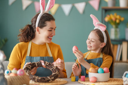Mother and her daughter painting eggs. Happy family preparing for Easter. Cute little child girl wearing bunny ears.の写真素材
