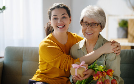 Beautiful young woman and her mother with flowers tulips in hands at home.の写真素材