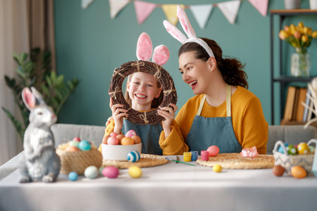 Mother and her daughter painting eggs. Happy family preparing for Easter. Cute little child girl wearing bunny ears.の写真素材