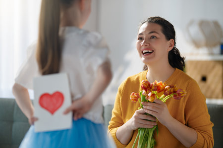 Happy mother's day. Child daughter congratulating mom and giving her flowers and postcard. Mum and girl smiling. Family holiday and togetherness.の写真素材