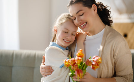 Happy mother's day. Child daughter is congratulating mom and giving her flowers. Mum and girl smiling and hugging. Family holiday and togetherness.の写真素材