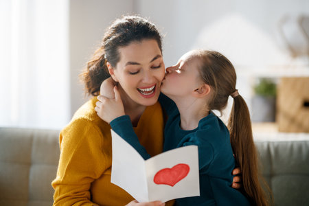 Happy mother's day. Child daughter is congratulating mom and giving her postcard. Mum and girl smiling and hugging. Family holiday and togetherness.の写真素材
